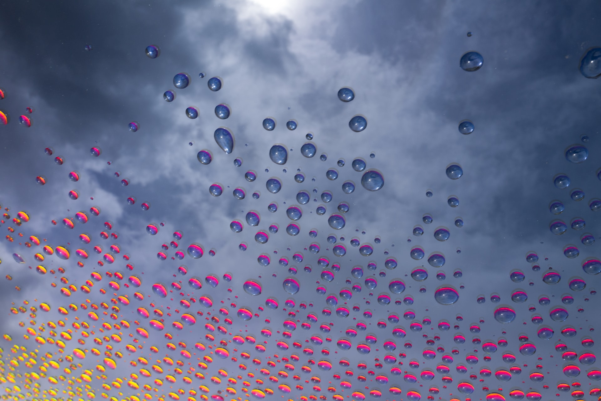 Water droplets against a cloudy blue-gray sky with pink and yellow reflections